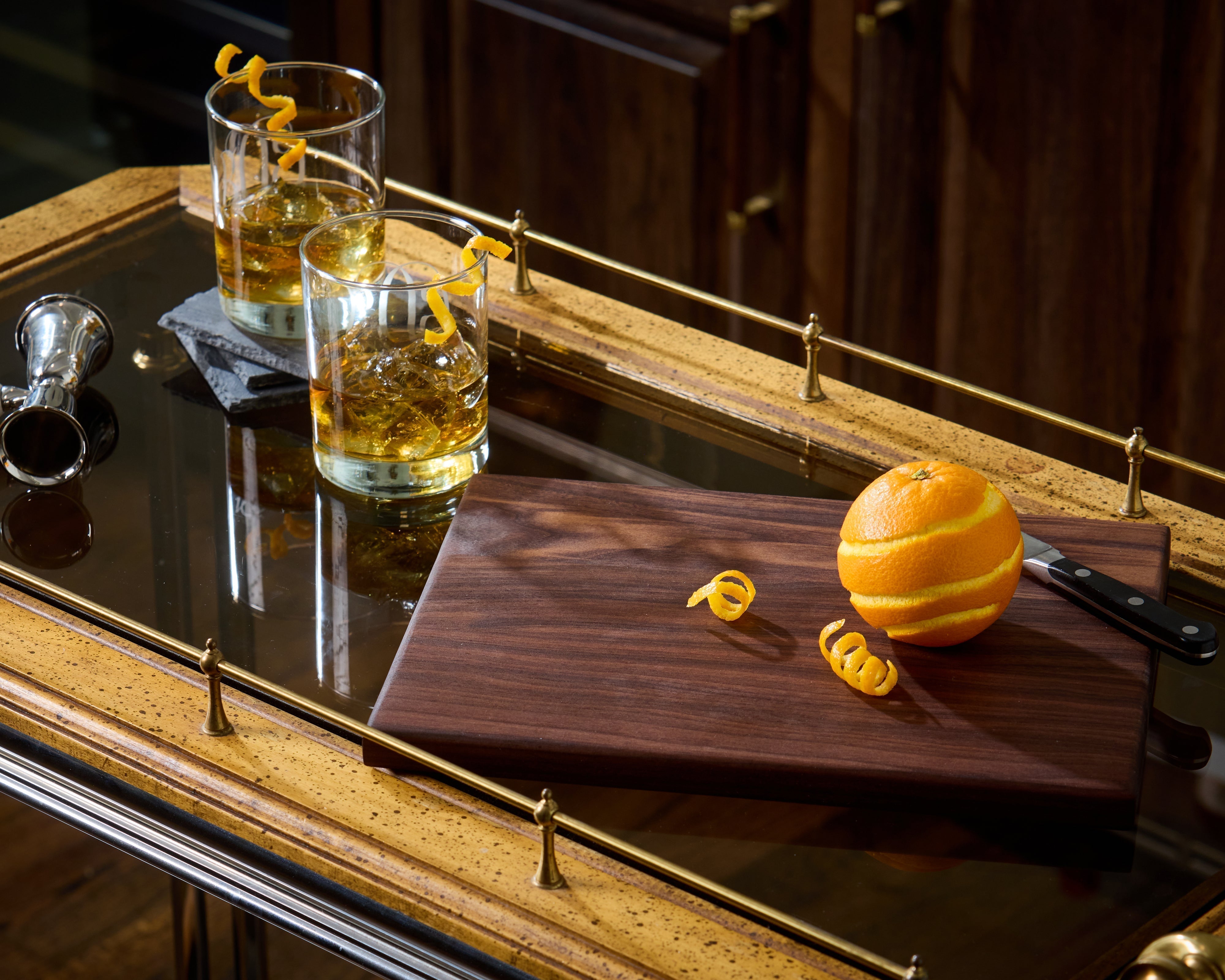 Wooden serving tray with whiskey glasses, orange, and knife on a bar table, perfect for stylish home wood decor.