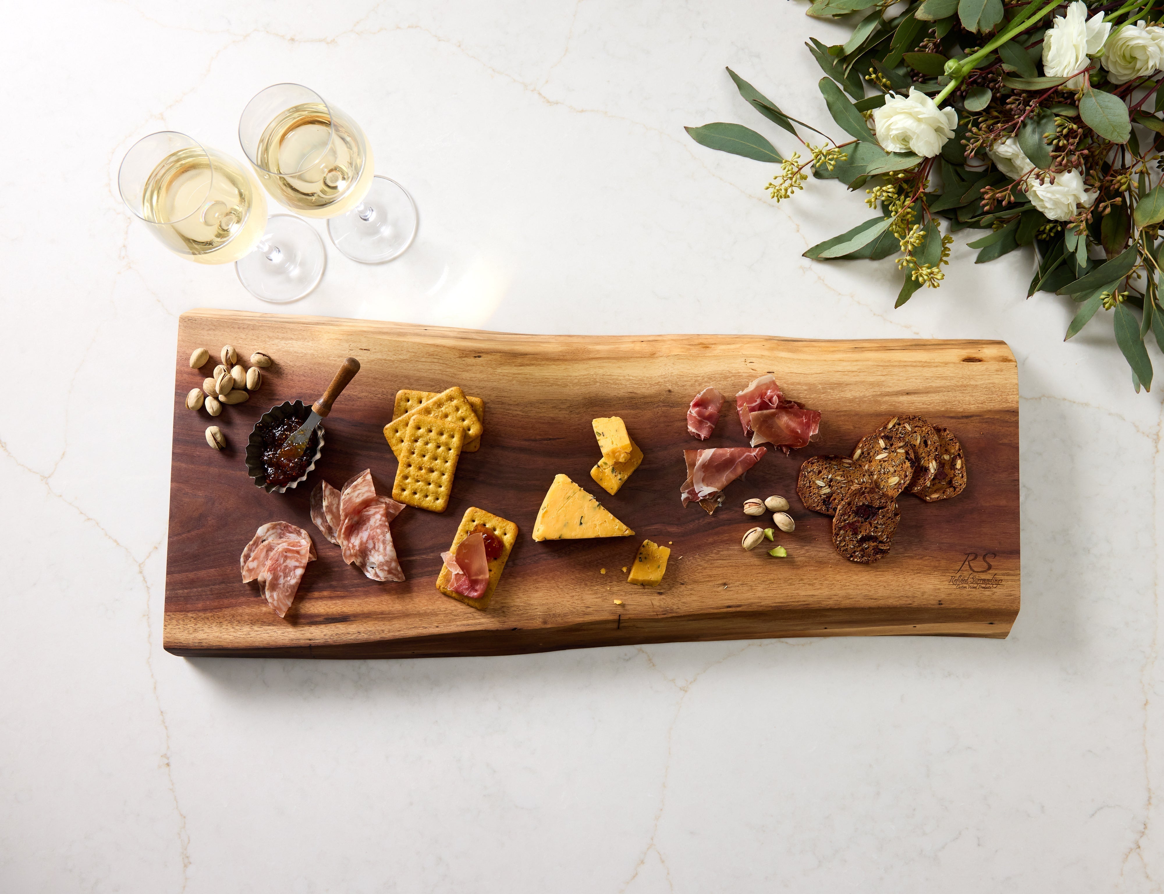 Live-edge custom charcuterie board by Refined Surroundings styled with crackers, cheese, jam & nuts for elegant board decor.