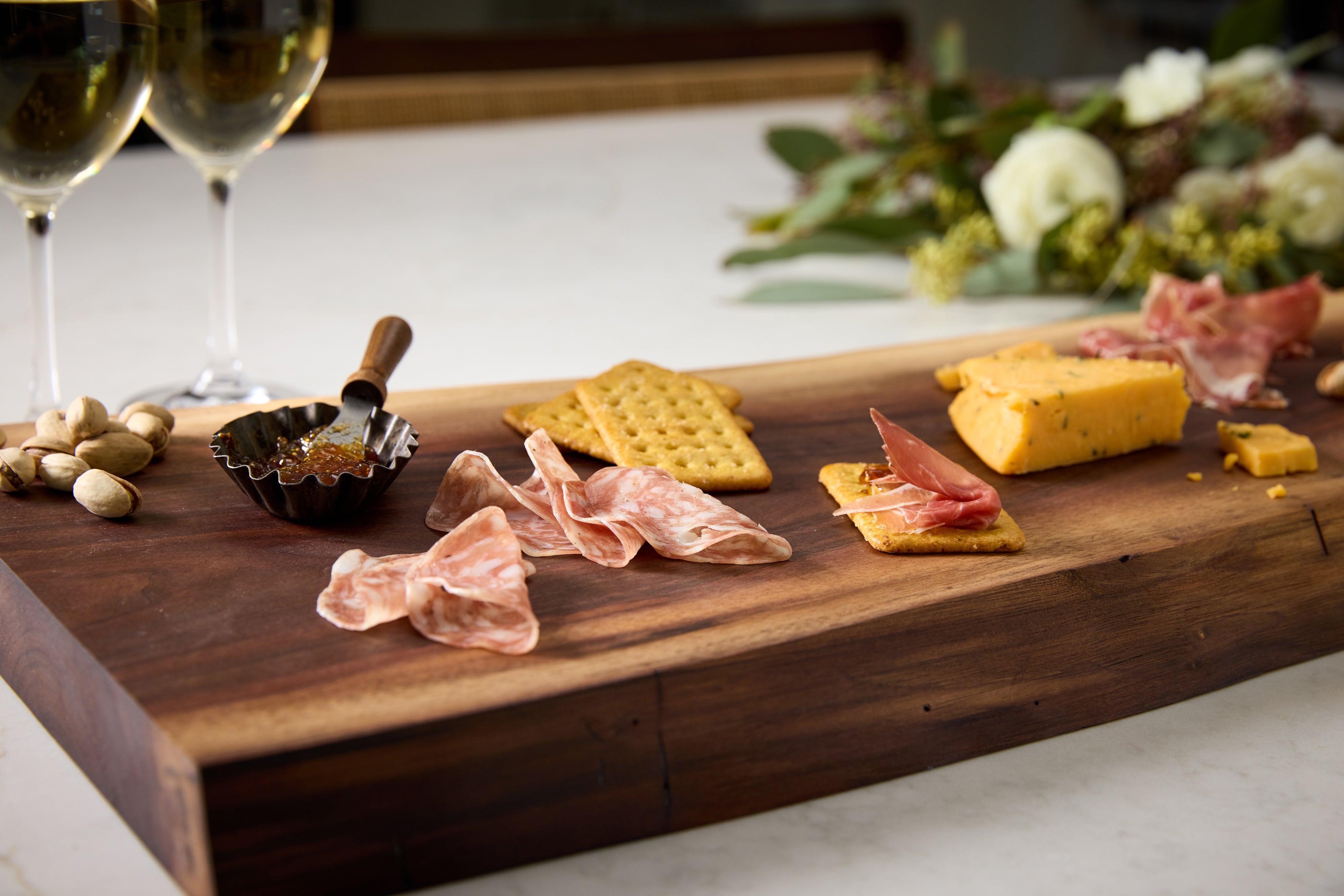 Custom live-edge charcuterie cutting board made of walnut, maple, and cherry with crackers, cheese, olives, and nuts spread on top.