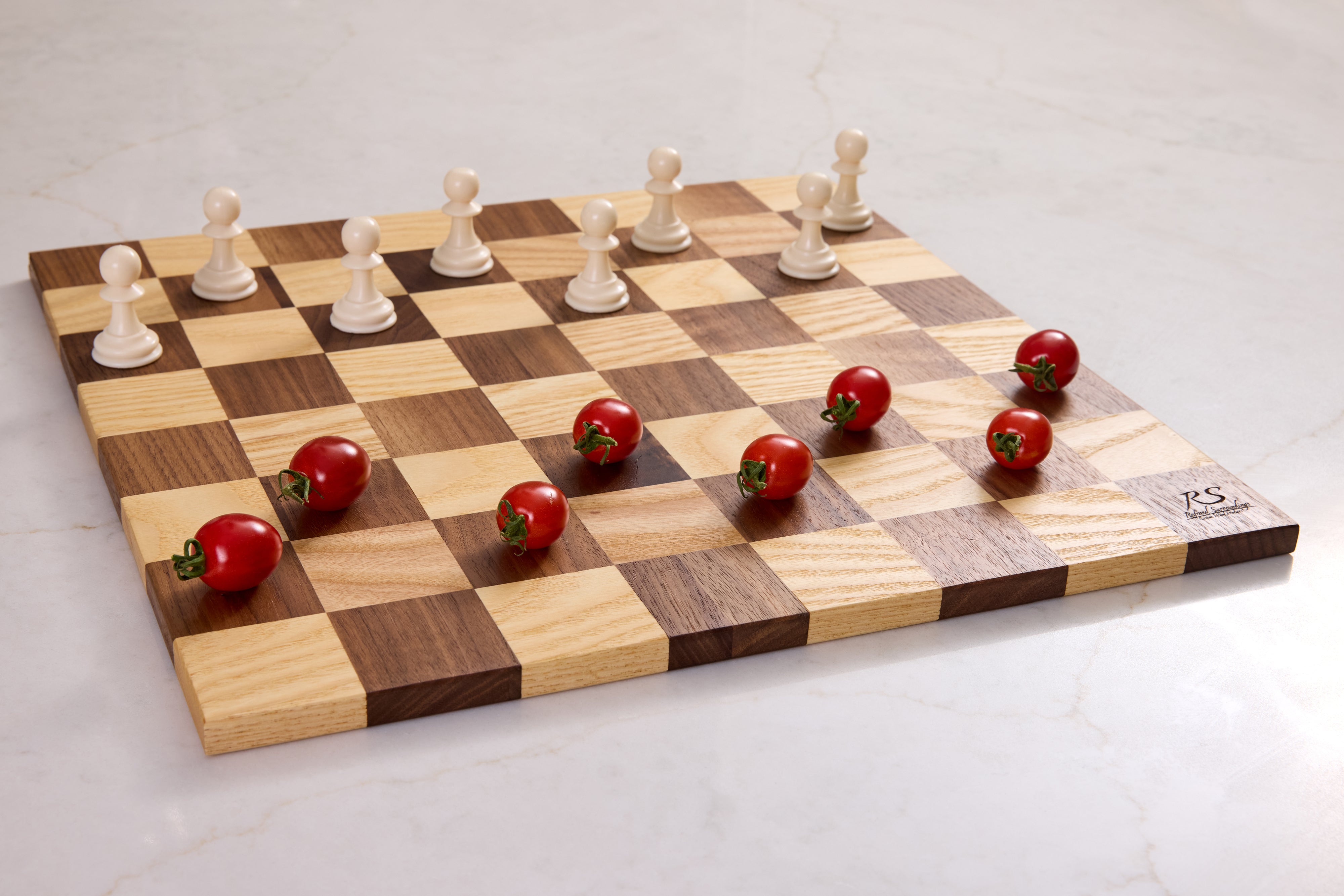 Wooden serving board in chessboard pattern of walnut and maple hardwood, styled with chess pawns and cherry tomatoes for décor