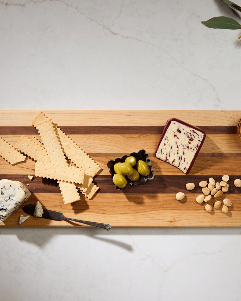 A combination of maple, cherry, and walnut wooden cutting boards displaying a charcuterie spread including cheese, and nuts.