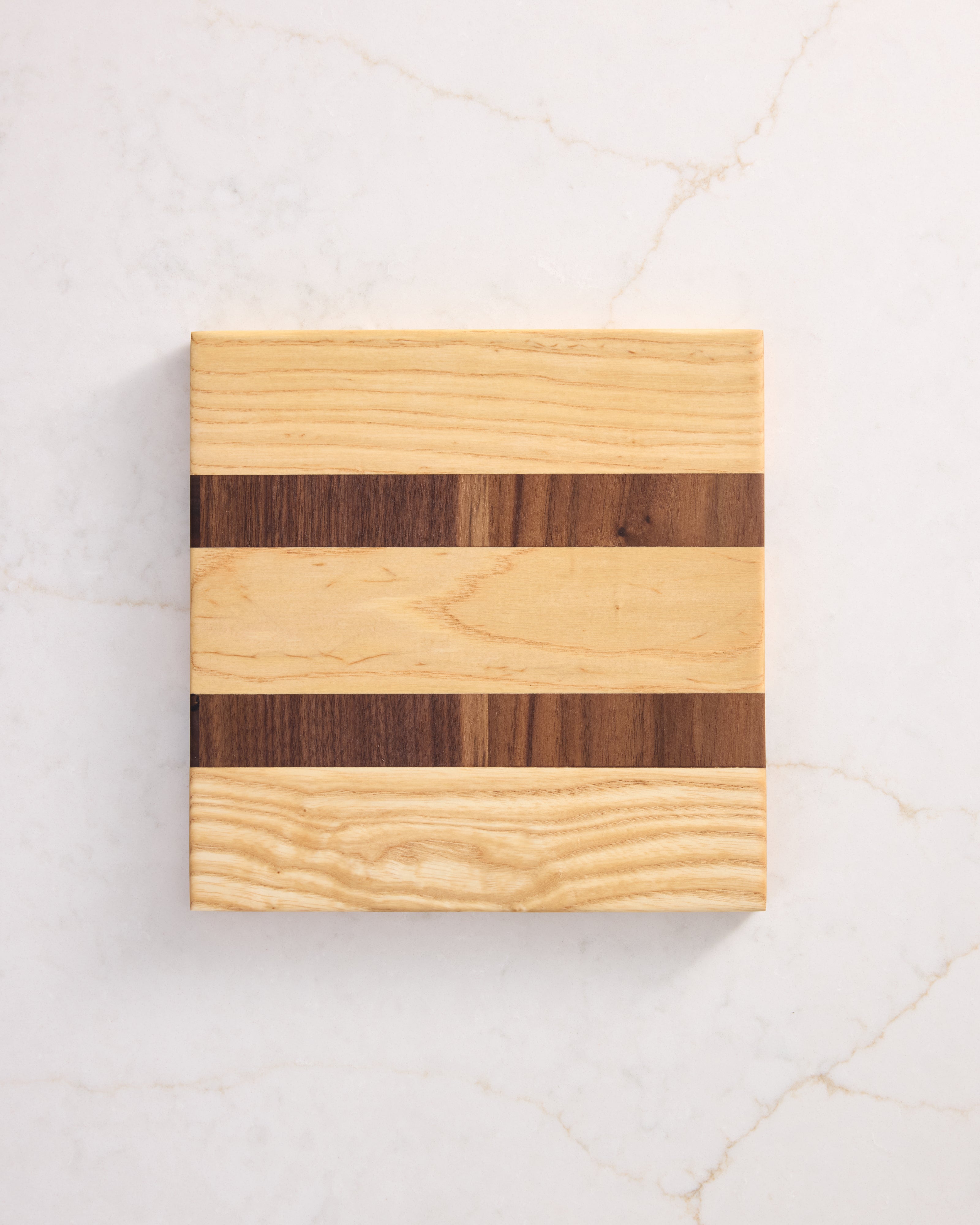 Top view of handcrafted maple and walnut cutting board on white marble — a small, elegant wooden board for garnish or prep.
