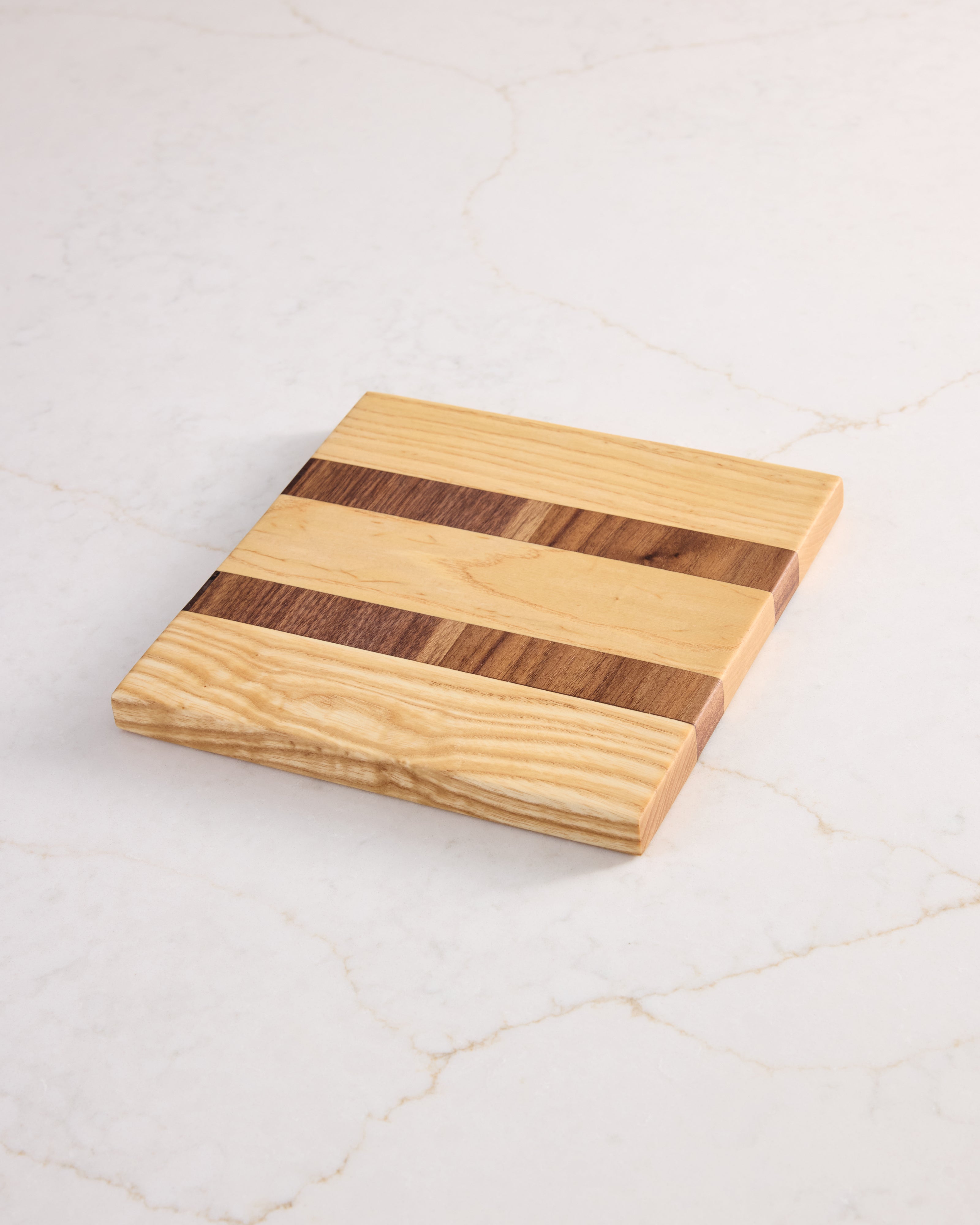 Minimalist wood garnish board made from maple and walnut, shown from above on white marble — perfect for clean kitchen prep.