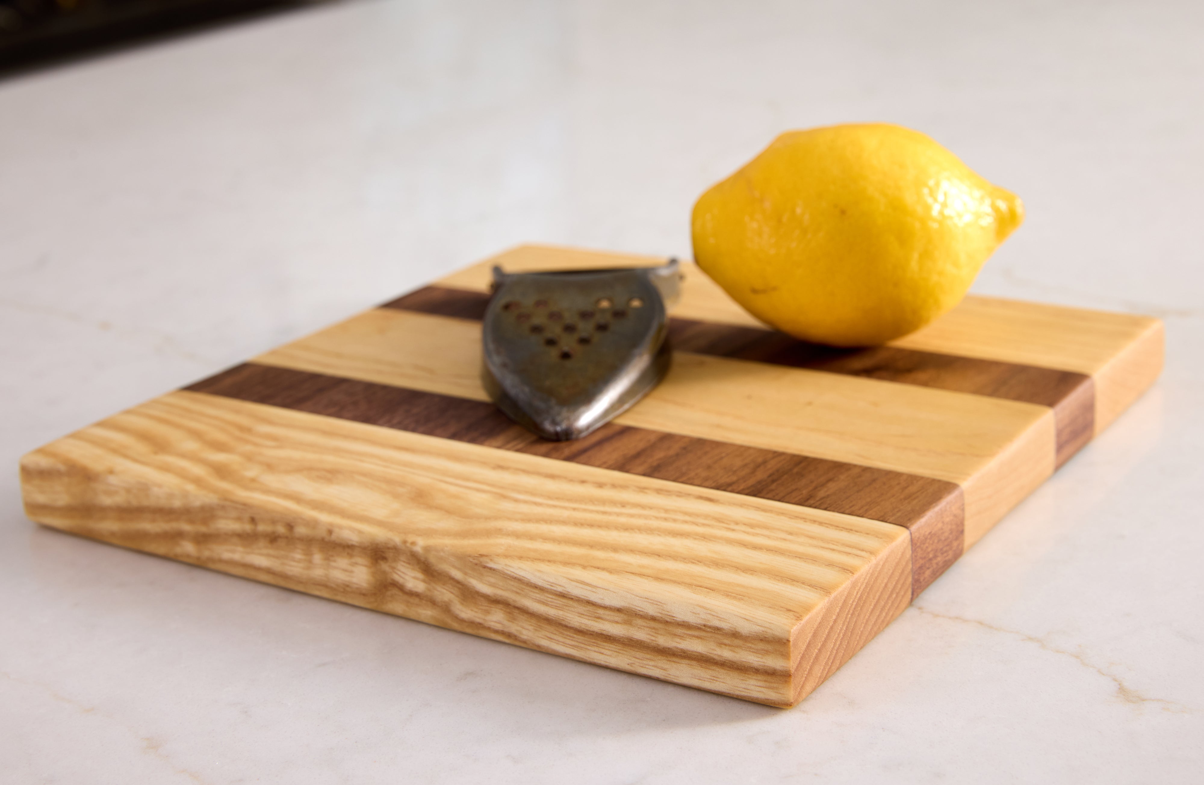 Compact maple and walnut cutting board with lemon and peeler — ideal for small prep tasks and elegant kitchen presentation.