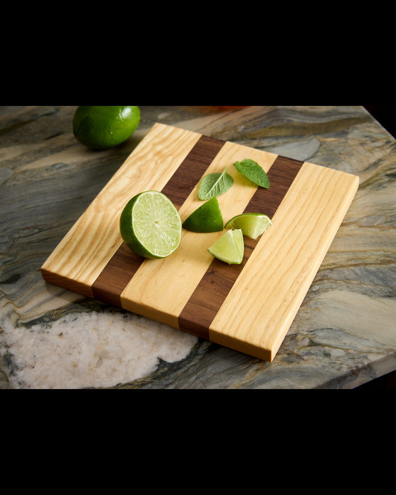 Close-up of maple and walnut garnish board with lime wedges and mint — a small, handcrafted wood cutting board for prep.