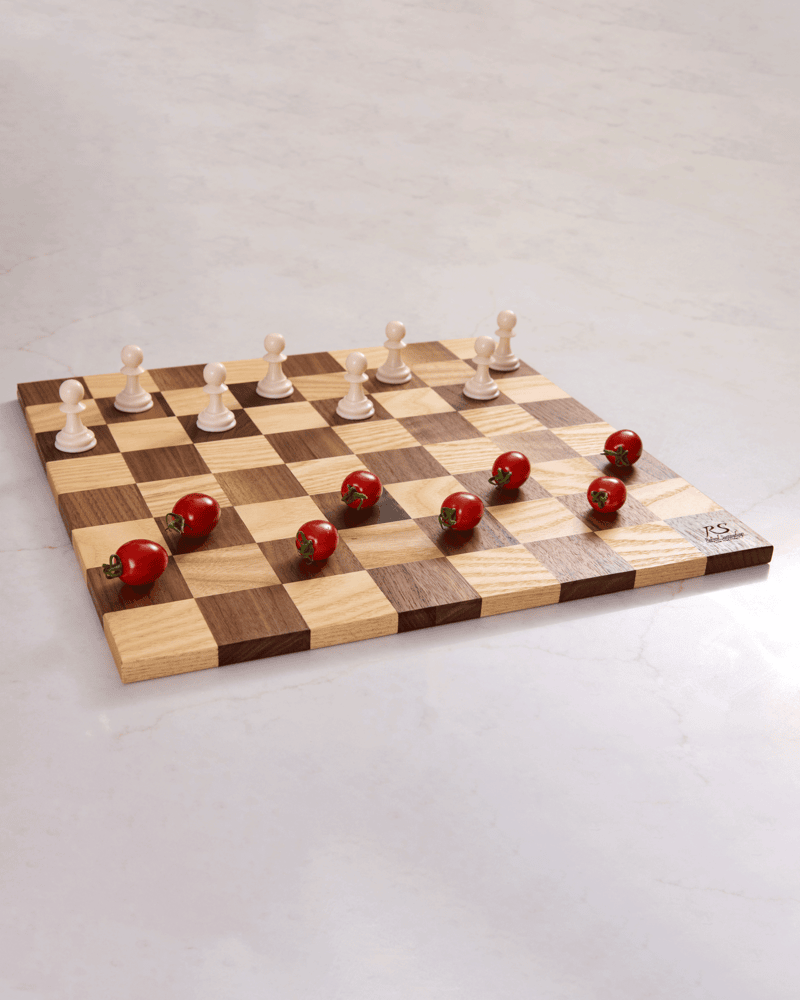Wood chess board in walnut and maple with cherry tomatoes and chess pieces, seen from the side — a unique decor element.