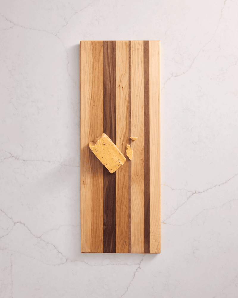 Close-up of walnut, cherry, and maple cutting board with a cheese block, showing wood grain and elegant serving functionality