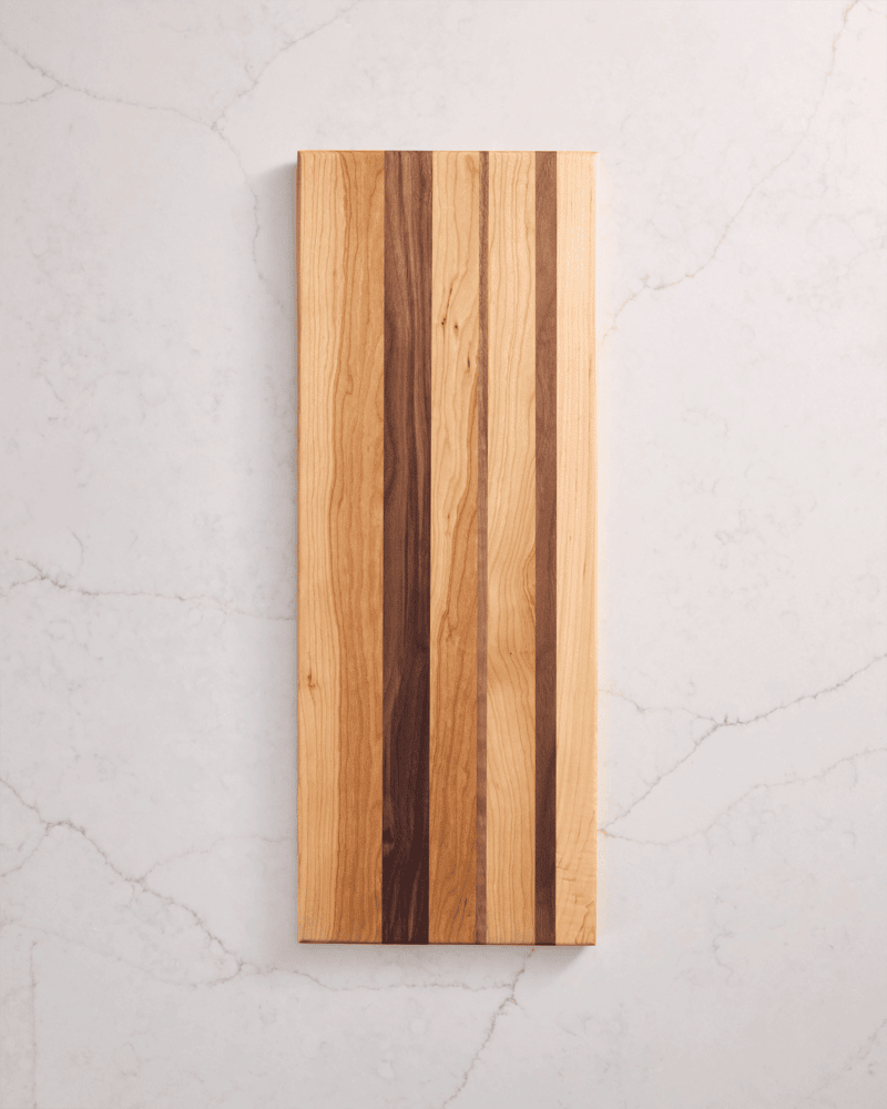 Close-up of a handcrafted walnut and maple cutting board on white marble, highlighting grain detail and premium wood finish.