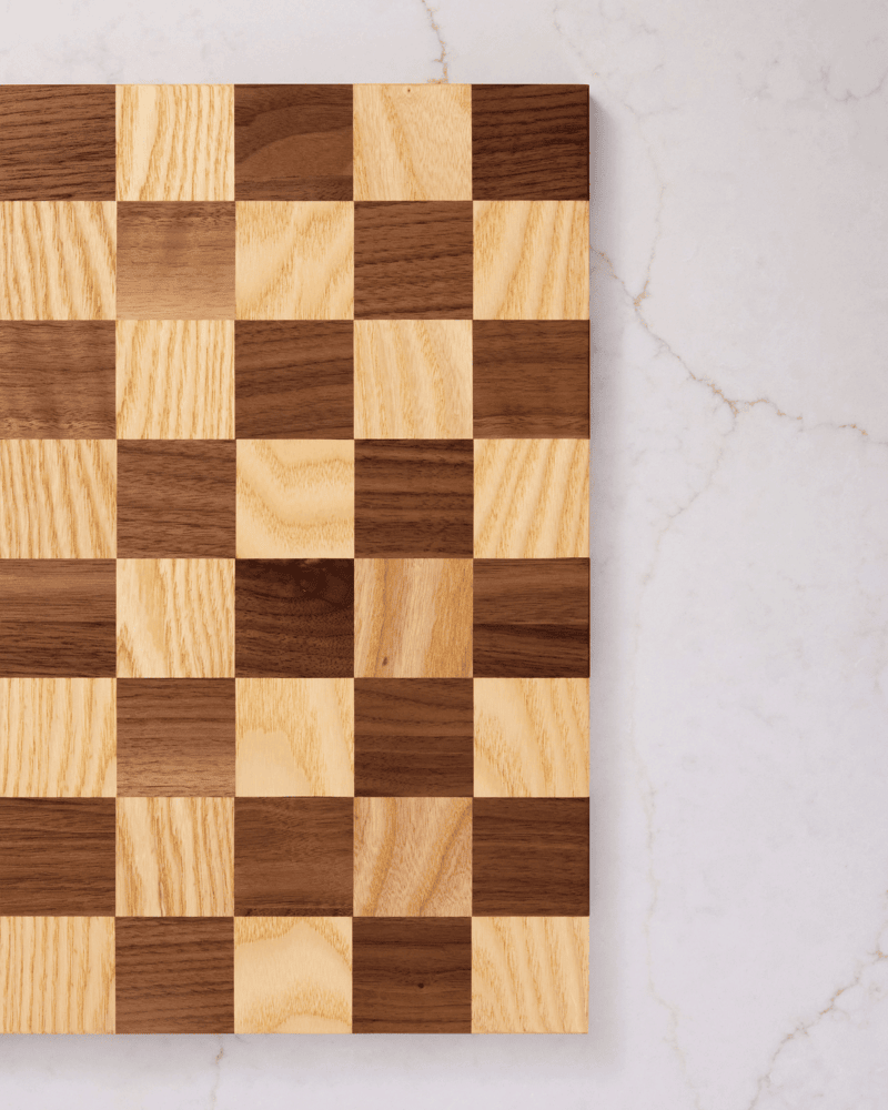 Right side of handmade maple and walnut chess board seen from above — minimalist wood decor on clean white marble.