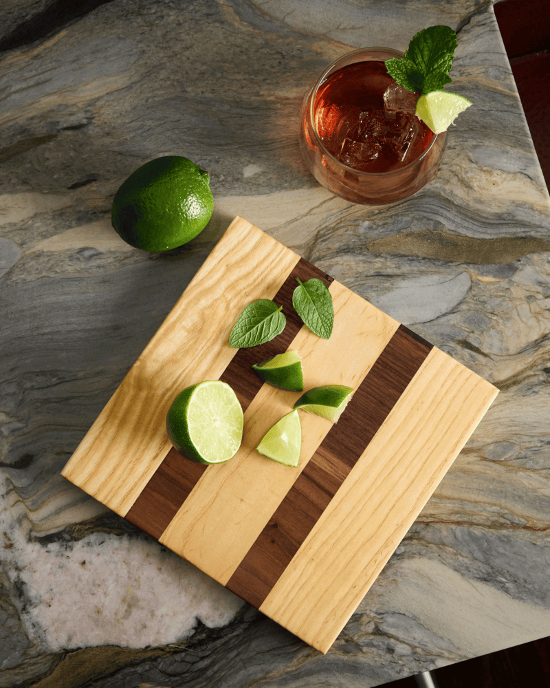 Maple and walnut garnish board styled with limes, mint, and cocktail — a perfect small wood cutting board for fresh prep.
