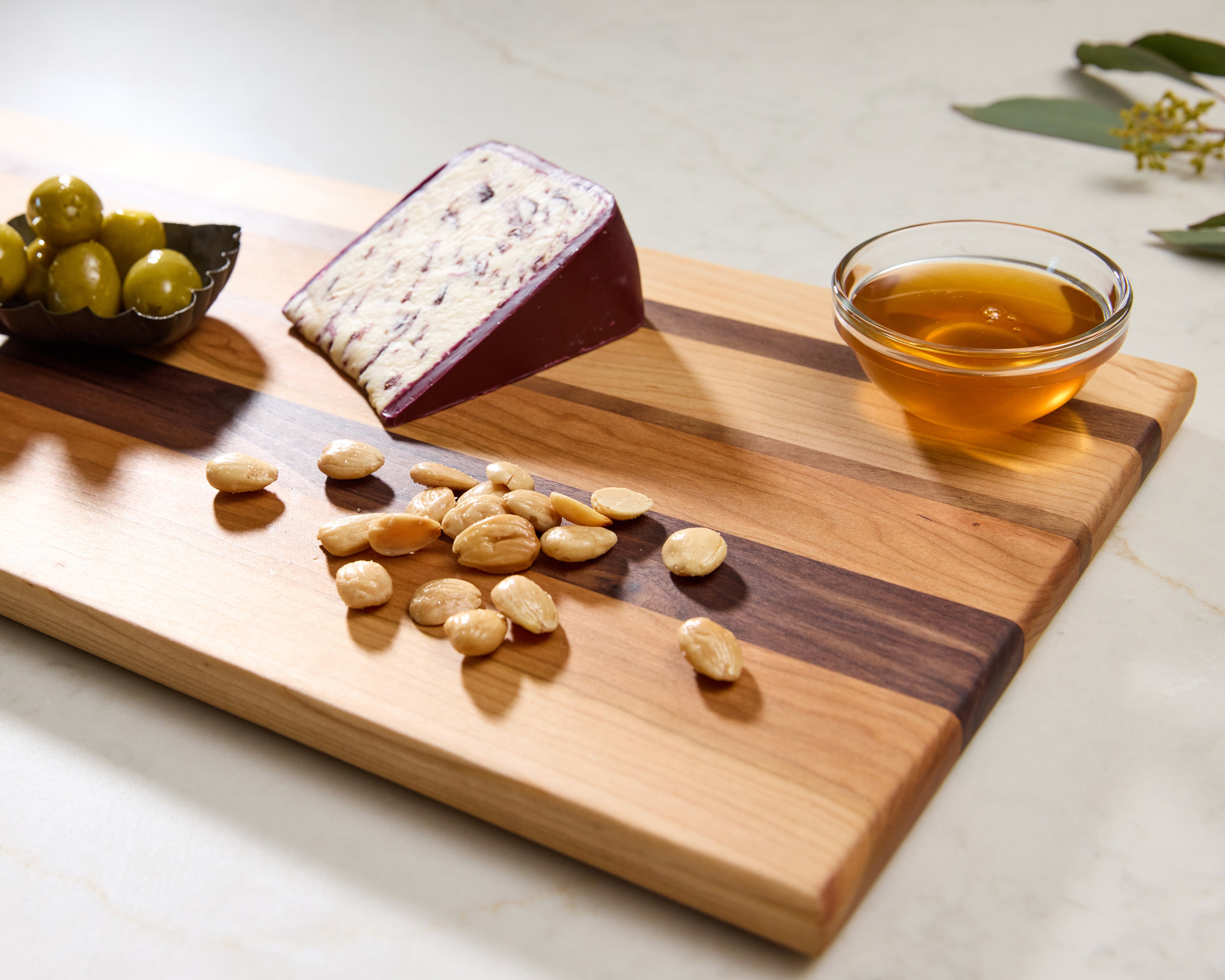 Maple and walnut wooden serving tray styled with olives, cheese, crackers, and marcona almonds on a marble surface