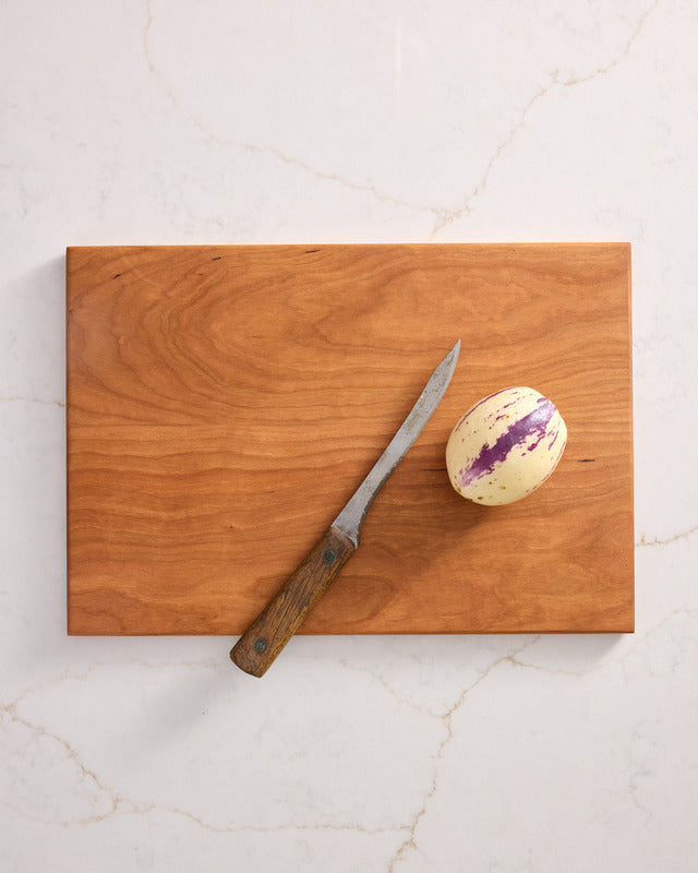 Medium cherry wood cutting board with smooth grain and red-brown tone, best chopping board and healthiest cutting board material.