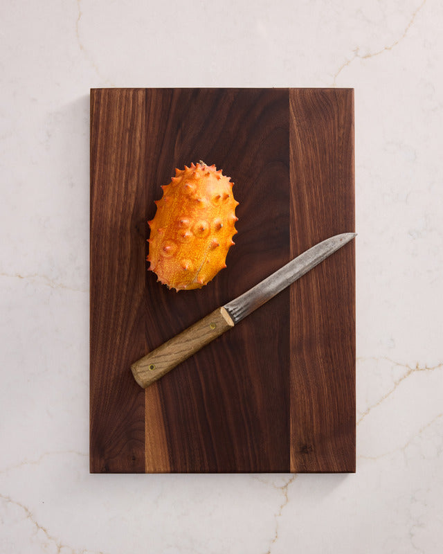 Medium rectangular walnut cutting board with sleek edges and polished wood finish, shown on a white marble counter.