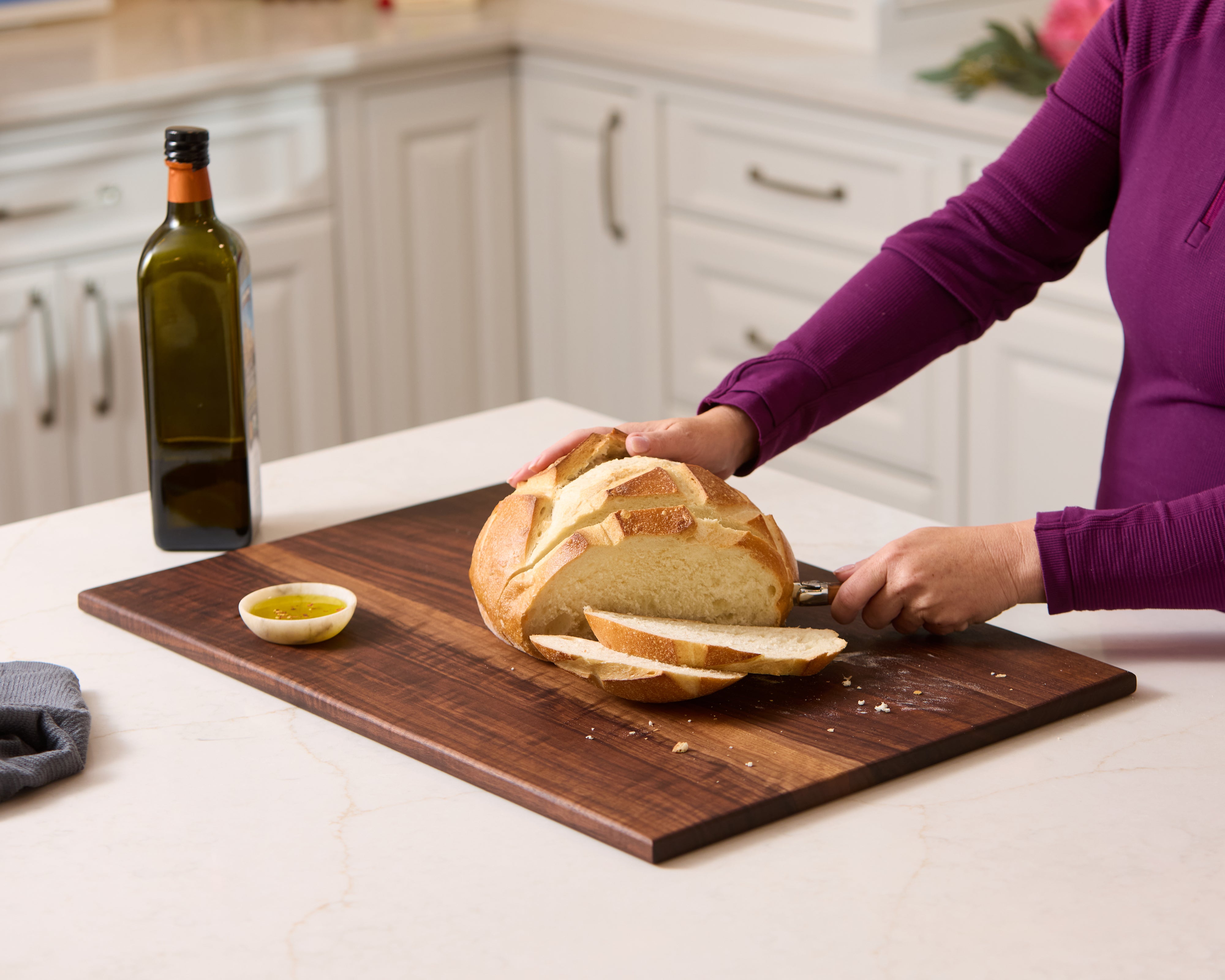 Medium walnut cutting board with loaf of bread being sliced, a durable best wooden chopping board and healthiest cutting board.