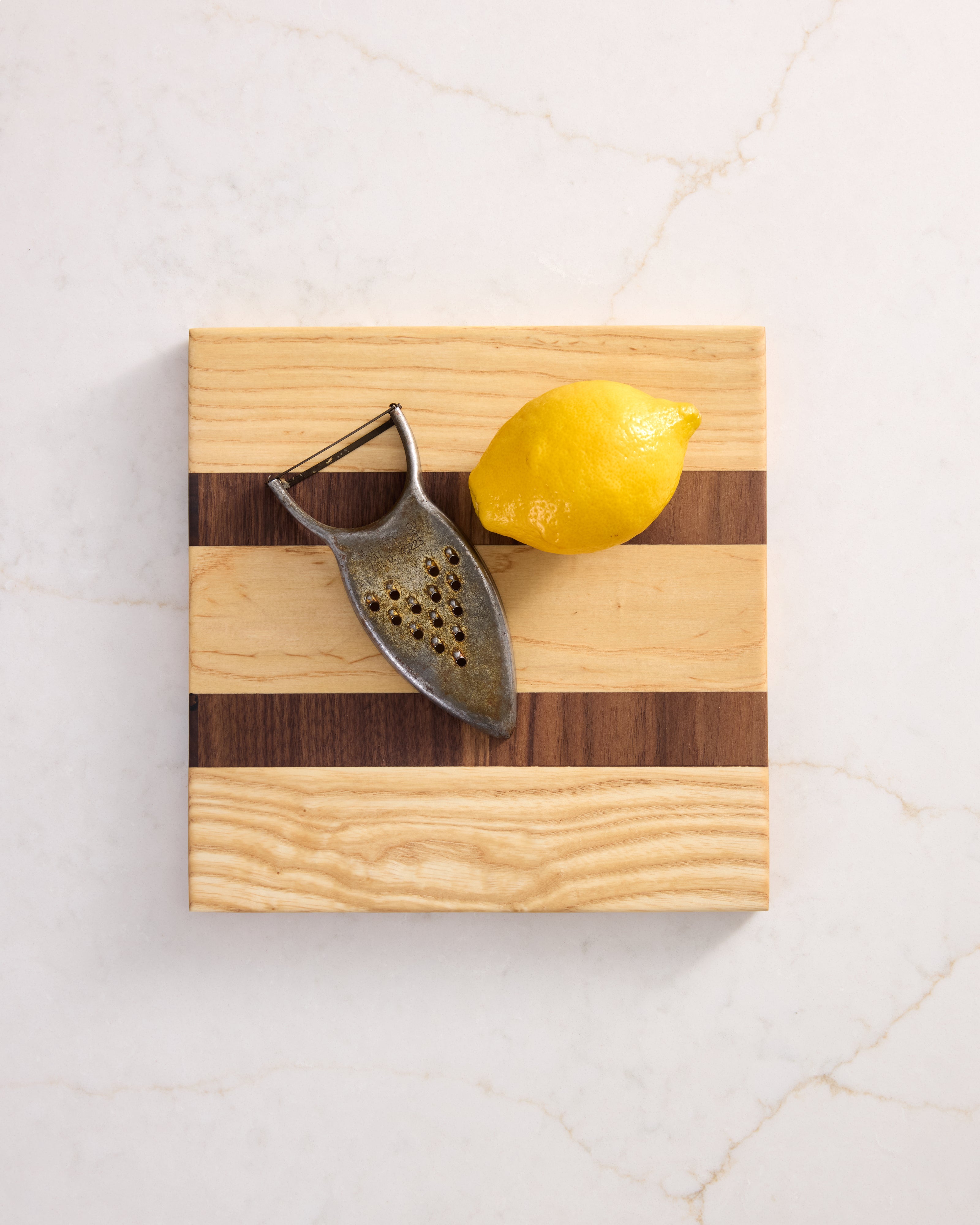 Maple and walnut cutting board with lemon and peeler — a compact and stylish wood board for prep, serving, or garnish work.