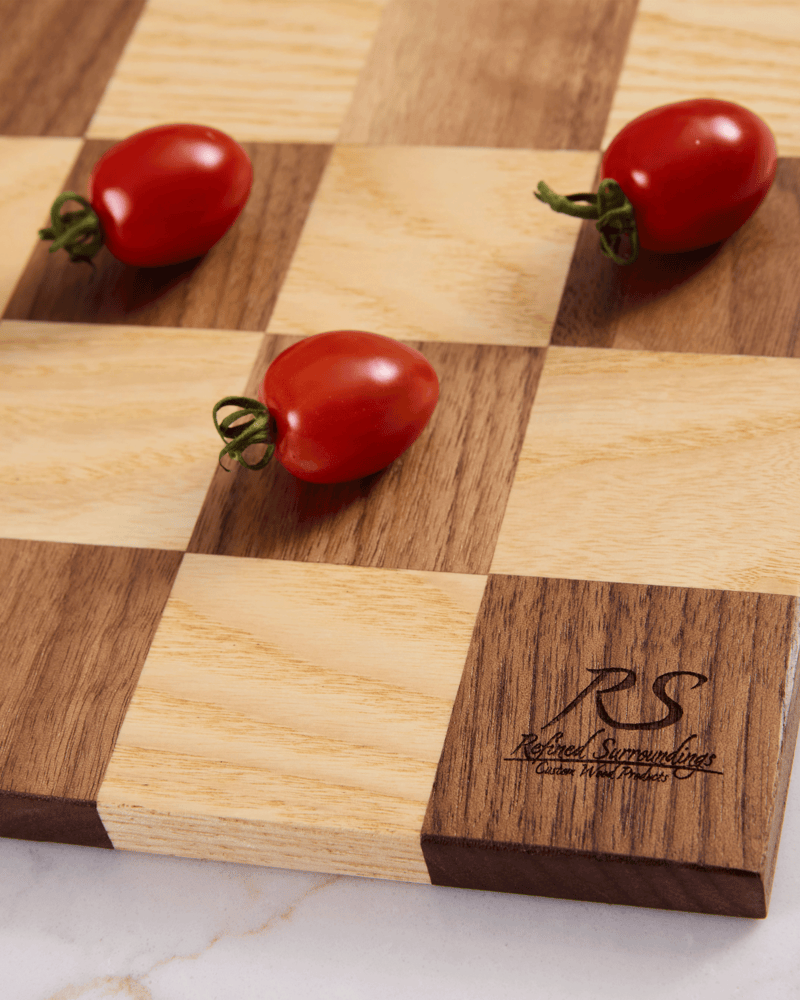 Detailed view of handmade chess board corner in walnut and maple with cherry tomatoes and branded logo on a square.