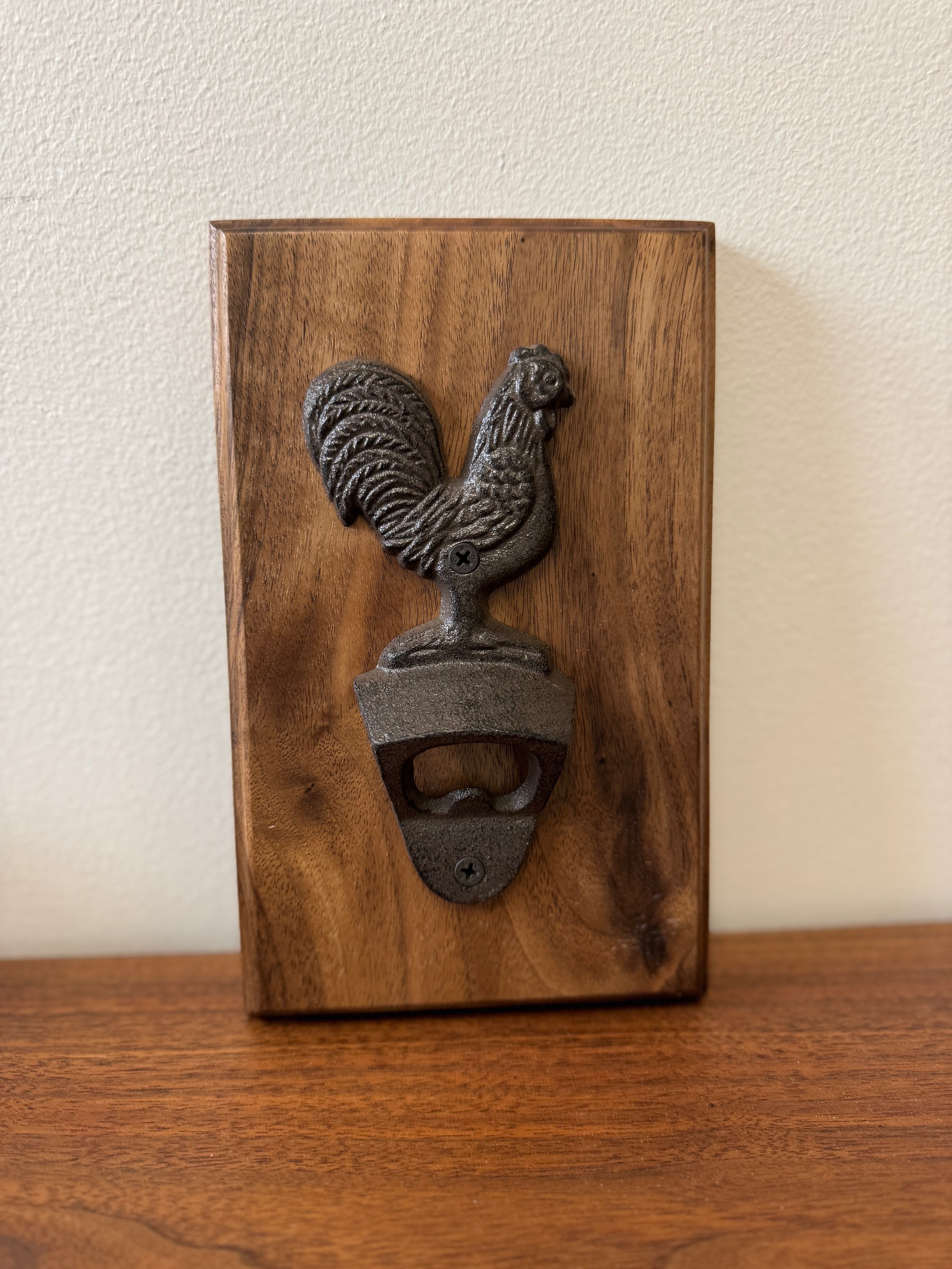 Walnut wood wall-mounted bottle opener with a cast iron rooster design, a rustic handcrafted accessory for kitchen or bar.